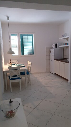 A small, bright kitchen with white cabinets, a dining table with chairs, and a window with blue shutters. - Villa Allegra in Lovran, Comfort Apartment 104, Balcony-Sea view (Lovran)