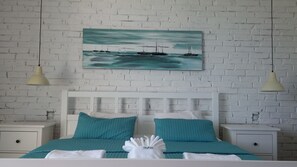 A bedroom with a white brick wall, a white bed frame, teal bedding, two bedside tables, and a painting of boats on the wall. - Villa Allegra in Lovran, Comfort Apartment 104, Balcony-Sea view (Lovran)