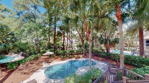 A swimming pool surrounded by palm trees and greenery, with a deck and lounge chairs.