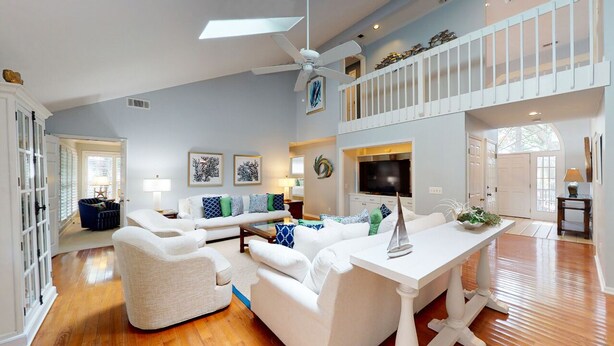 A spacious living room with a white sofa set, a coffee table, and a TV. There is a balcony with a railing and a door leading to another room. - Beach Access Across the Street! (Hilton Head)