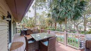 A covered outdoor patio with wicker furniture, a glass table, and a pool in the background. - Beach Access Across the Street! (Hilton Head)