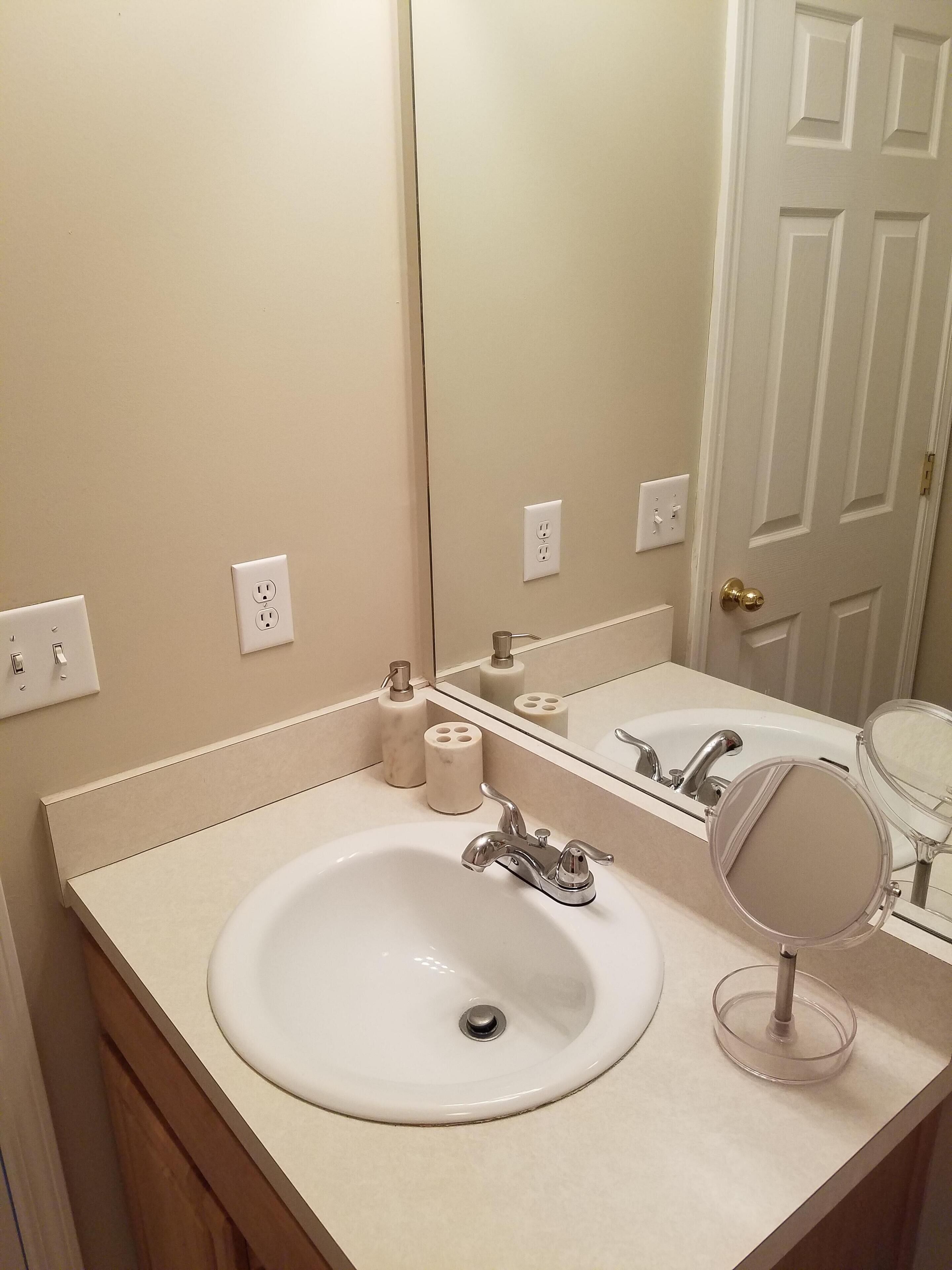 A bathroom with a white sink, a mirror, and a toilet paper holder.
