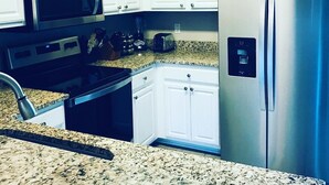 Una cocina con armarios blancos, un refrigerador de acero inoxidable, un microondas y una encimera de granito.
