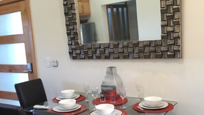 Un espace repas avec une table en verre, des chaises noires et un miroir doté d’un cadre à motifs.