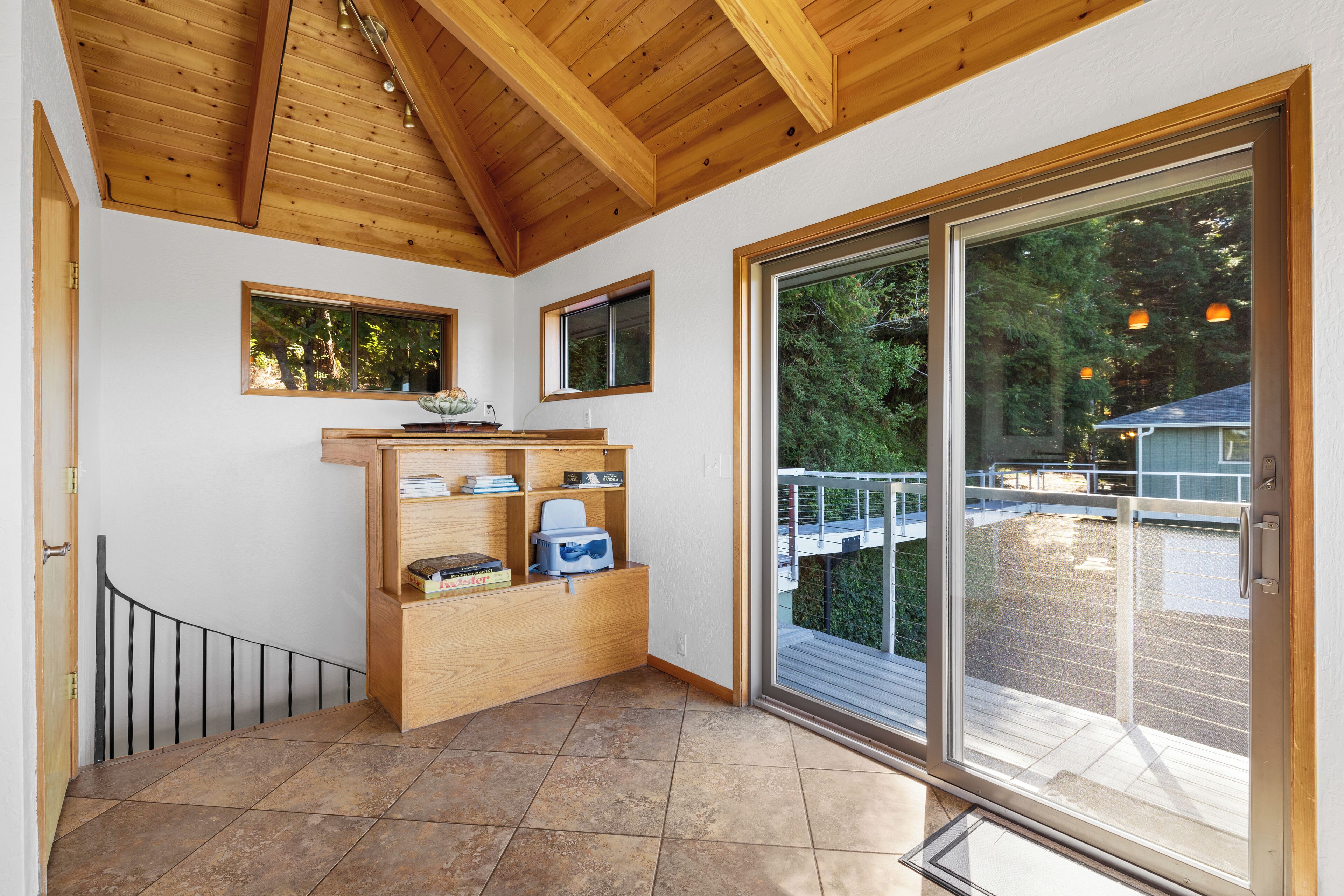 A room with a wooden ceiling, a sliding glass door to a balcony, and a built-in wooden shelf with books and a printer.
