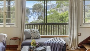 A cozy room with a large window, a sofa, a small table with a vase of flowers, and a view of a natural landscape. - Mandala Bruny Island, waterfront, near Restaurant (Alonnah)