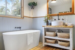 A bathroom with a freestanding bathtub, a wooden vanity with a sink, and a mirror above it. - Mandala Bruny Island, waterfront, near Restaurant (Alonnah)