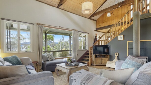 A spacious living room with a large window, a staircase, and a television. - Mandala Bruny Island, waterfront, near Restaurant (Alonnah)