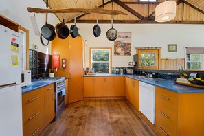 A kitchen with wooden cabinets, a stove, and hanging pots. - Mandala Bruny Island, waterfront, near Restaurant (Alonnah)