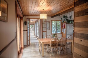 A wooden interior with a dining area featuring a table and chairs, a hanging light fixture, and a refrigerator. - Mandala Bruny Island, waterfront, near Restaurant (Alonnah)