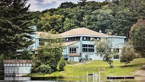 A large, two-story building with a flat roof, surrounded by a lake and dense trees. - In the Estates, close to Owl's Nest, new kitchen, amazing views, minutes off I93 (Thornton)