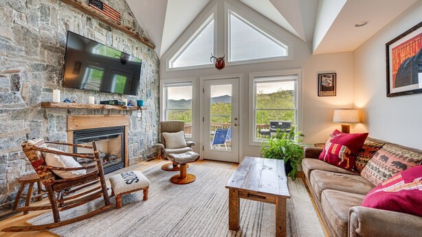 A cozy living room with a stone fireplace, a large TV, and a comfortable seating area with a couch and chairs. - In the Estates, close to Owl's Nest, new kitchen, amazing views, minutes off I93 (Thornton)