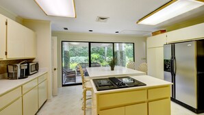 A modern kitchen with a central island, a refrigerator, and a view of greenery through large windows. - Excellent Cottage Location on Sea Island (Sea Island)