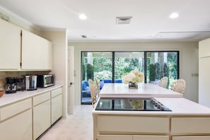 Een moderne keuken met een centraal eiland, inbouwapparatuur en uitzicht op een tuin via een schuifdeur.
