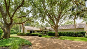 A house with a driveway leading to a garage, surrounded by mature trees and well-maintained lawns. - Excellent Cottage Location on Sea Island (Sea Island)