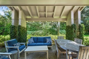 Een terras buiten met een overdekte zithoek, inclusief een bank en stoelen, en een houten tafel.