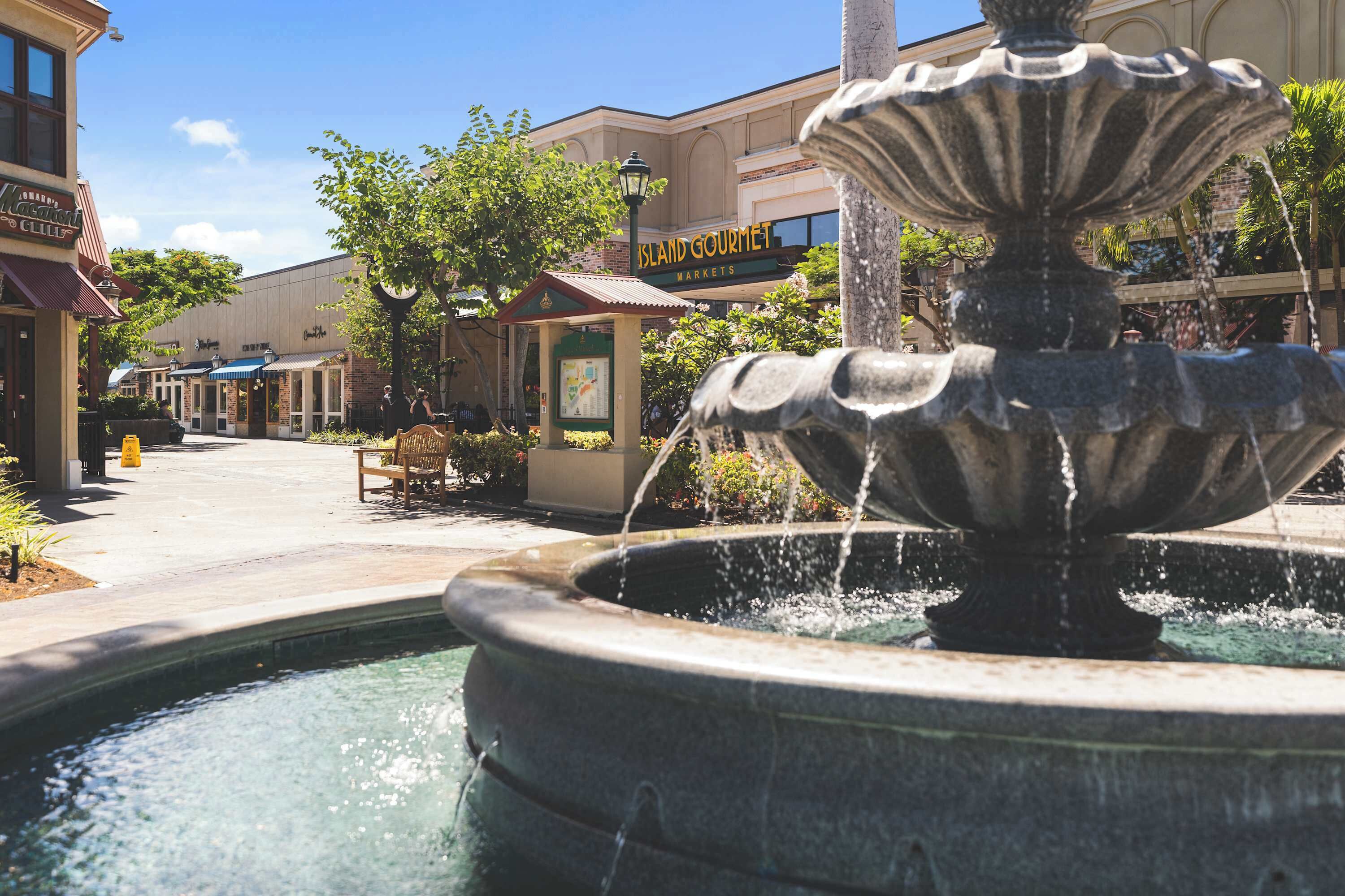A fountain in a public square with a building labeled "Island Gourmet Markets" in the background.