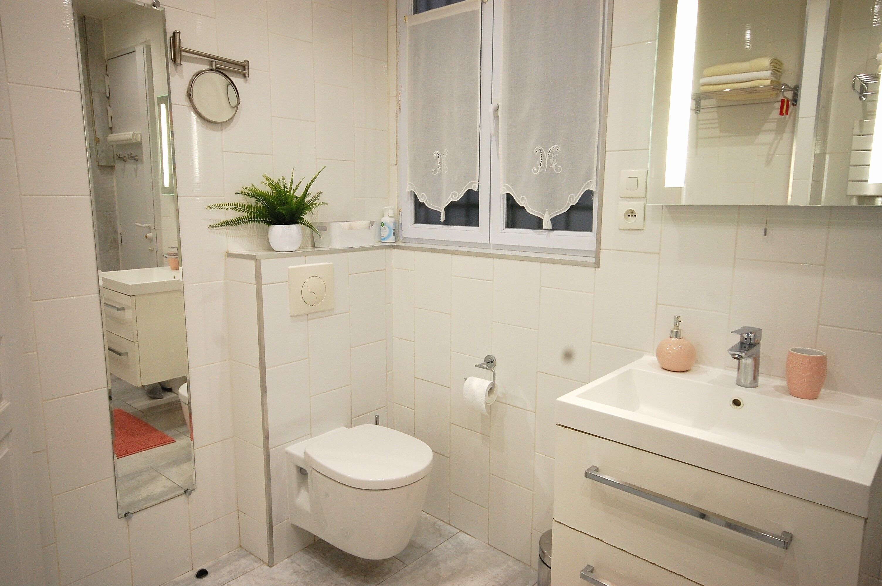 A bathroom with a toilet, sink, and mirror. There is a plant on the counter and a towel rack above the sink.