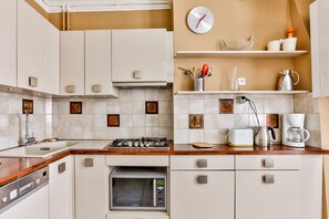 A modern kitchen with white cabinets, a wooden countertop, a built-in oven, a coffee maker, and a clock on the wall.