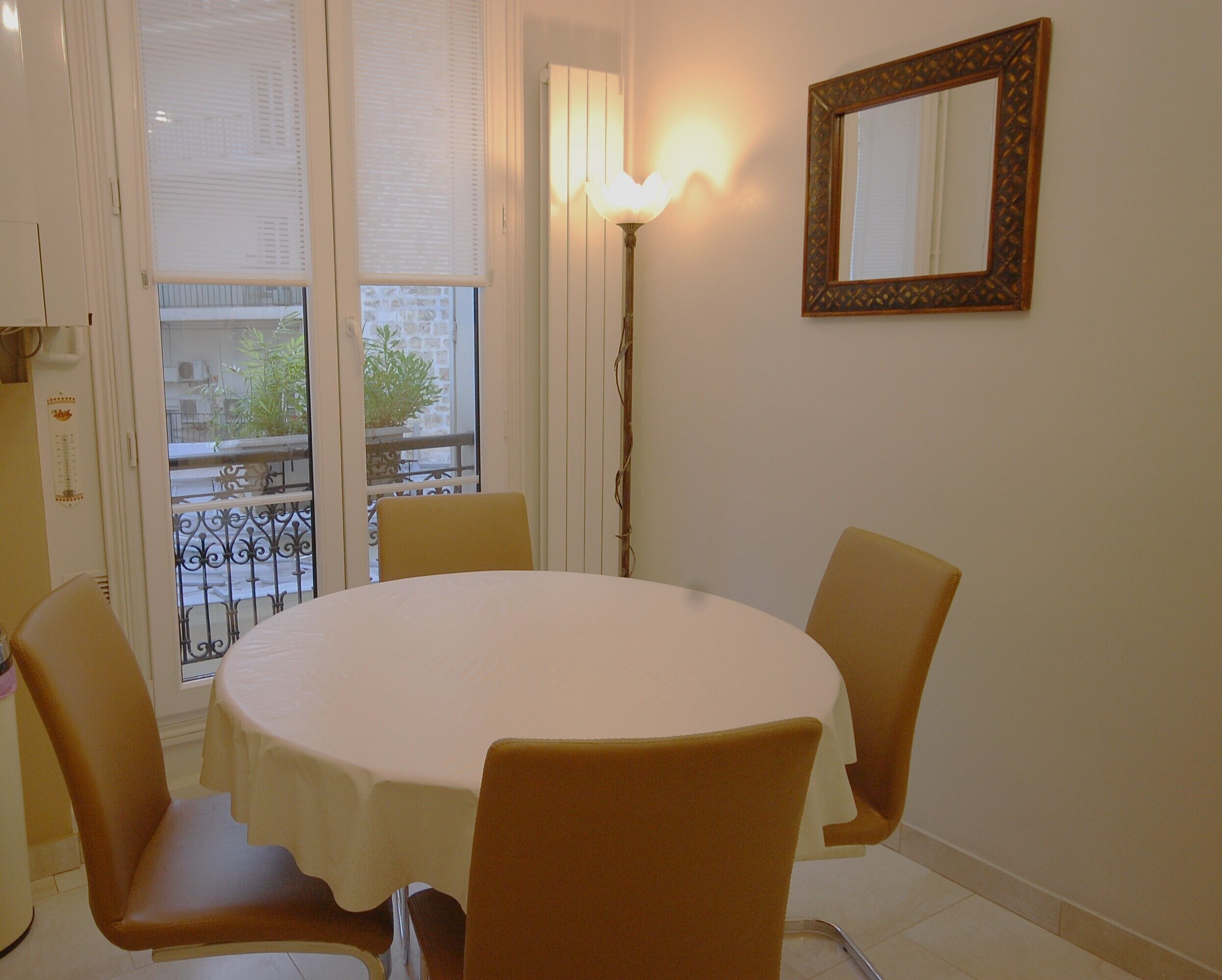 A dining area with a round table and four chairs, a wall-mounted mirror, and a floor lamp.