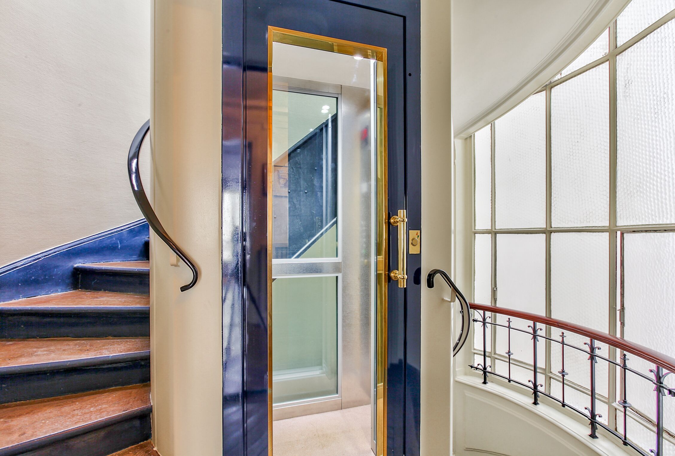 A staircase with a dark blue door, a handrail, and a view of a room with a window.