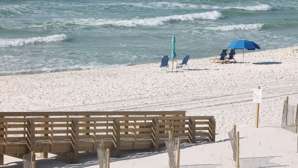 Una spiaggia con panchine di legno e due ombrelloni blu.