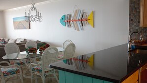 Una cucina con isola verde acqua, sedie in vimini bianco e un tavolo da pranzo.