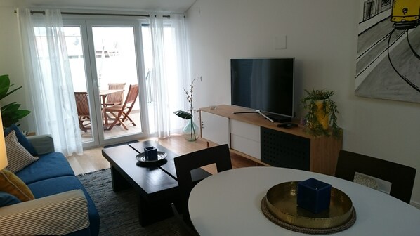 A modern living room with a sofa, a coffee table, a TV, and a dining area with a table and chairs.