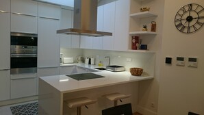 Eine moderne Küche mit weißen Schränken, einem eingebauten Ofen, einer Kaffeemaschine und einer Wanduhr.