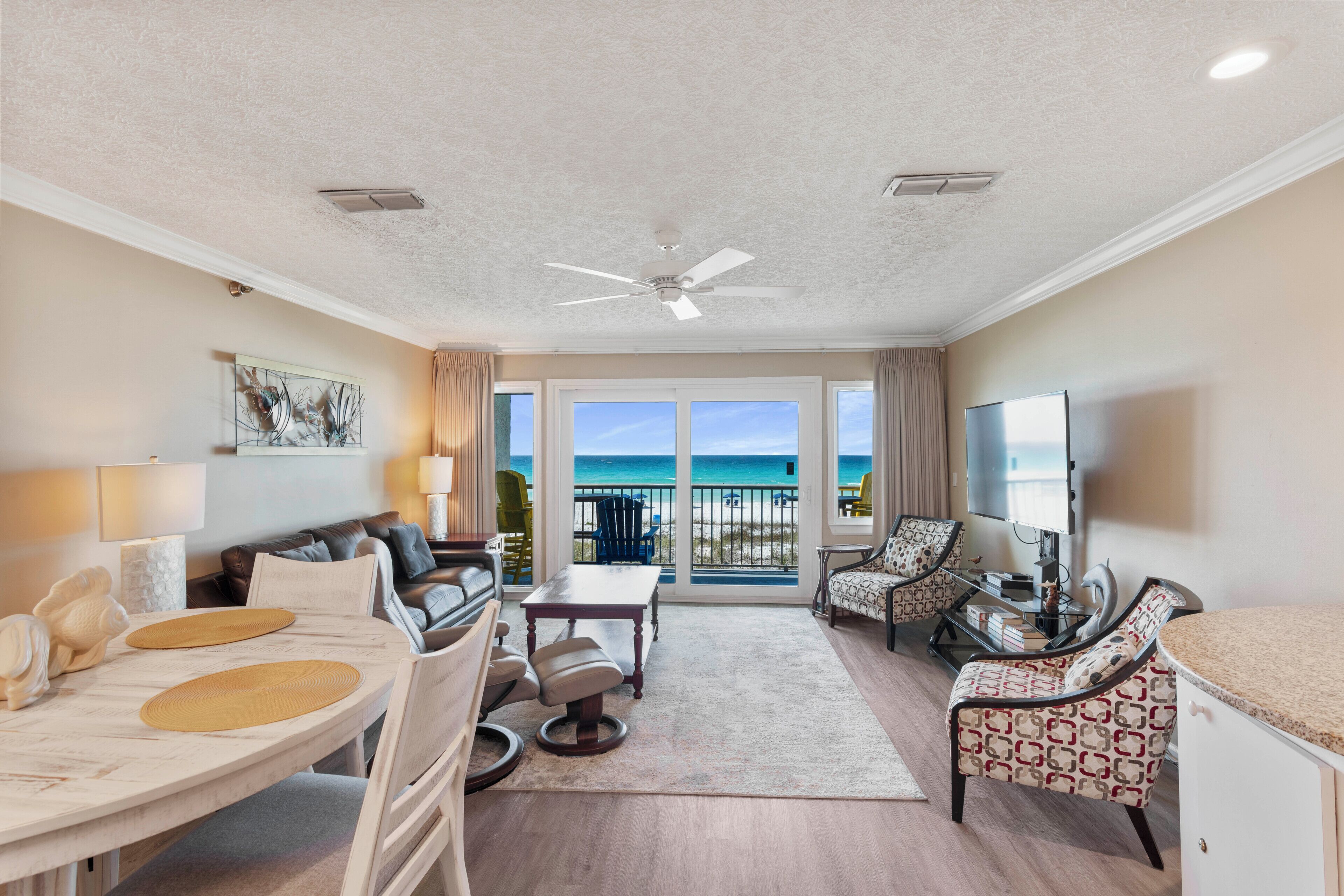 A spacious living area with a balcony, a ceiling fan, and a television.