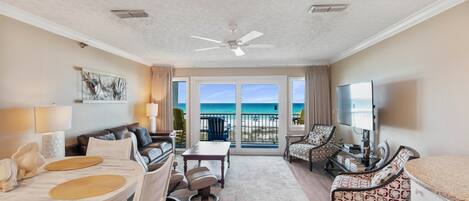 A spacious living area with a balcony, a ceiling fan, and a television.