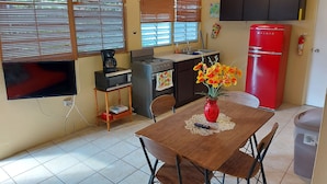 A compact kitchen with a stove, microwave, and red refrigerator. A dining table with chairs is in the center, and a vase with flowers is on the table.