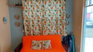 A room with a bed, a curtain with a floral pattern, a wall clock, and a door leading outside.