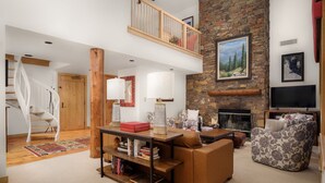 A spacious living room with a high ceiling, a fireplace, a staircase, and a cozy seating area. - RMR: Cody House C Condo in Teton Village (Teton Village)