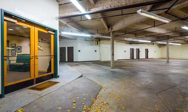 An indoor parking garage with concrete floors and walls, fluorescent lighting, and a glass door entrance labeled "PRIVATE RESIDENCES."