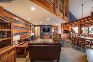 A spacious living area with a large brown leather sofa, wooden cabinets, and a dining table with chairs.