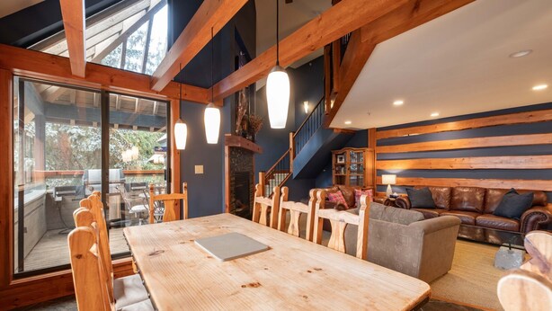 Ein Holzespeisesaal mit Stühlen, ein Sofa und ein Kamin in einem Raum mit freiliegenden Holzbalken und einer Treppe.