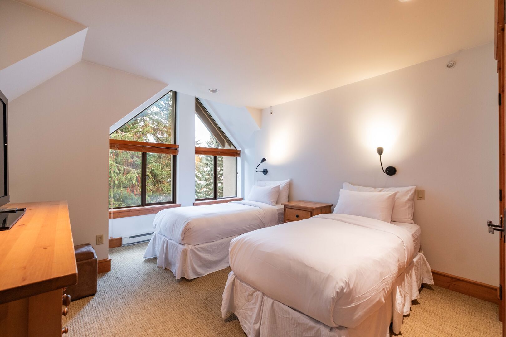 Une chambre avec deux lits, un bureau et une grande fenêtre donnant sur les arbres.