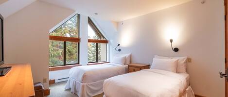 Une chambre avec deux lits, un bureau et une grande fenêtre donnant sur les arbres.