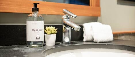 A bathroom sink with a hand soap dispenser, a small potted plant, and a white towel.