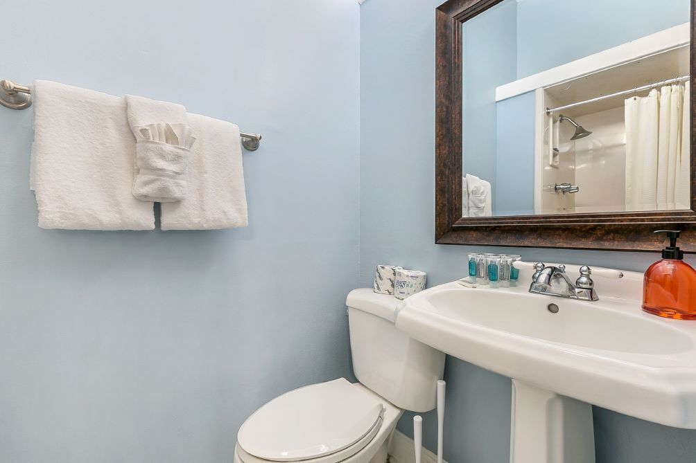 Un baño con inodoro blanco, un lavabo con espejo y un perchero con dos toallas.