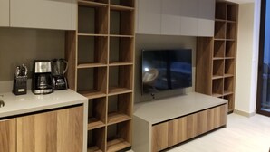 Ett modernt kök med inbyggda träskåp, en bänkskiva med en kaffebryggare och en platt-TV som är monterad på väggen.