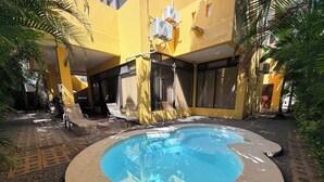 Piscina circular com um deck ao redor, paredes amarelas e aparelhos de ar condicionado.
