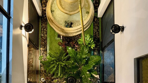 Um edifício moderno com um espelho d'água central, rodeado por vegetação exuberante e detalhes em pedra.