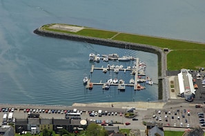 Vista aérea de un puerto deportivo con barcos amarrados, un estacionamiento y edificios en primer plano.