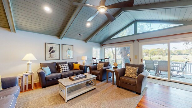 A spacious living room with a high ceiling, ceiling fan, and large windows offering a view of the outdoors. - Golf course and lagoon views! (Hilton Head)