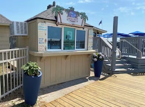 A small ice cream stand with a menu board, located on a wooden deck with potted plants.