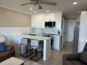 Una cocina moderna con armarios blancos, una isla central con taburetes, un microondas, una estufa y un refrigerador.