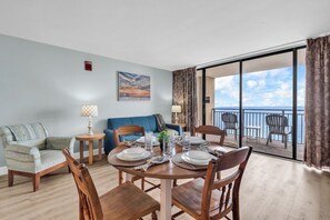 Un coin repas avec une table ronde dressée pour quatre personnes, un canapé et un balcon avec des chaises.