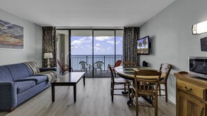 Een moderne woonkamer met een bank, eettafel, stoelen, een televisie en een balkon met uitzicht op zee.